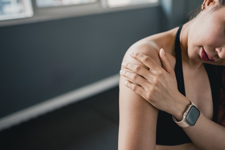Female athlete holding painful shoulder after workout representing rotator cuff injury, muscle strain, sports trauma and orthopedic health problems.